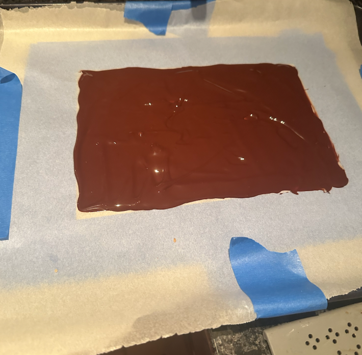 Melted chocolate spread over parchment paper.